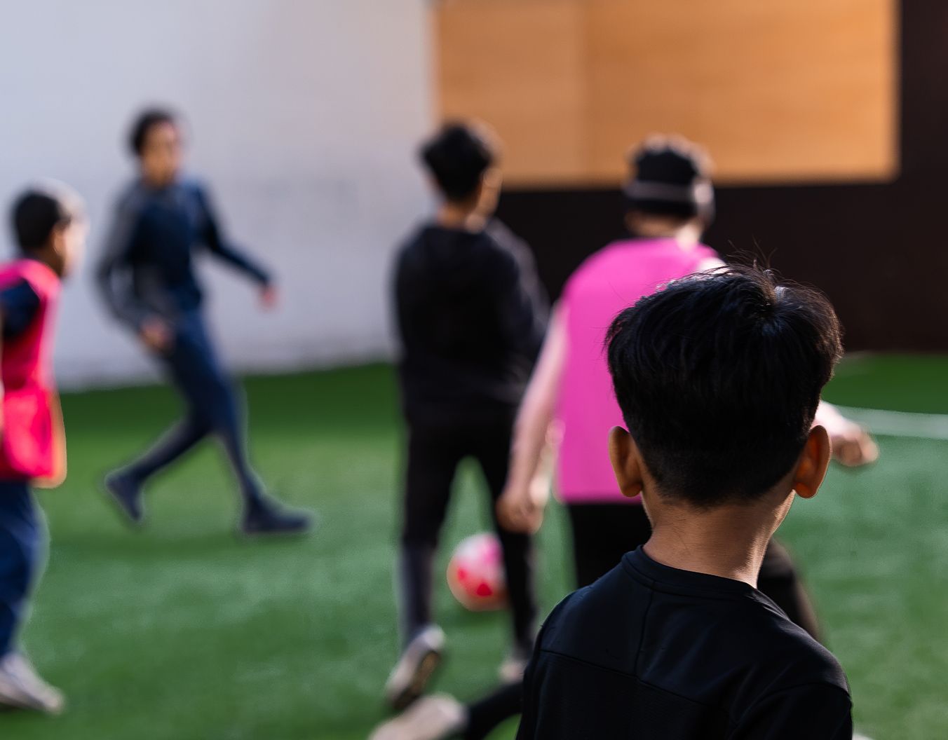 young children playing football on an astroturf field