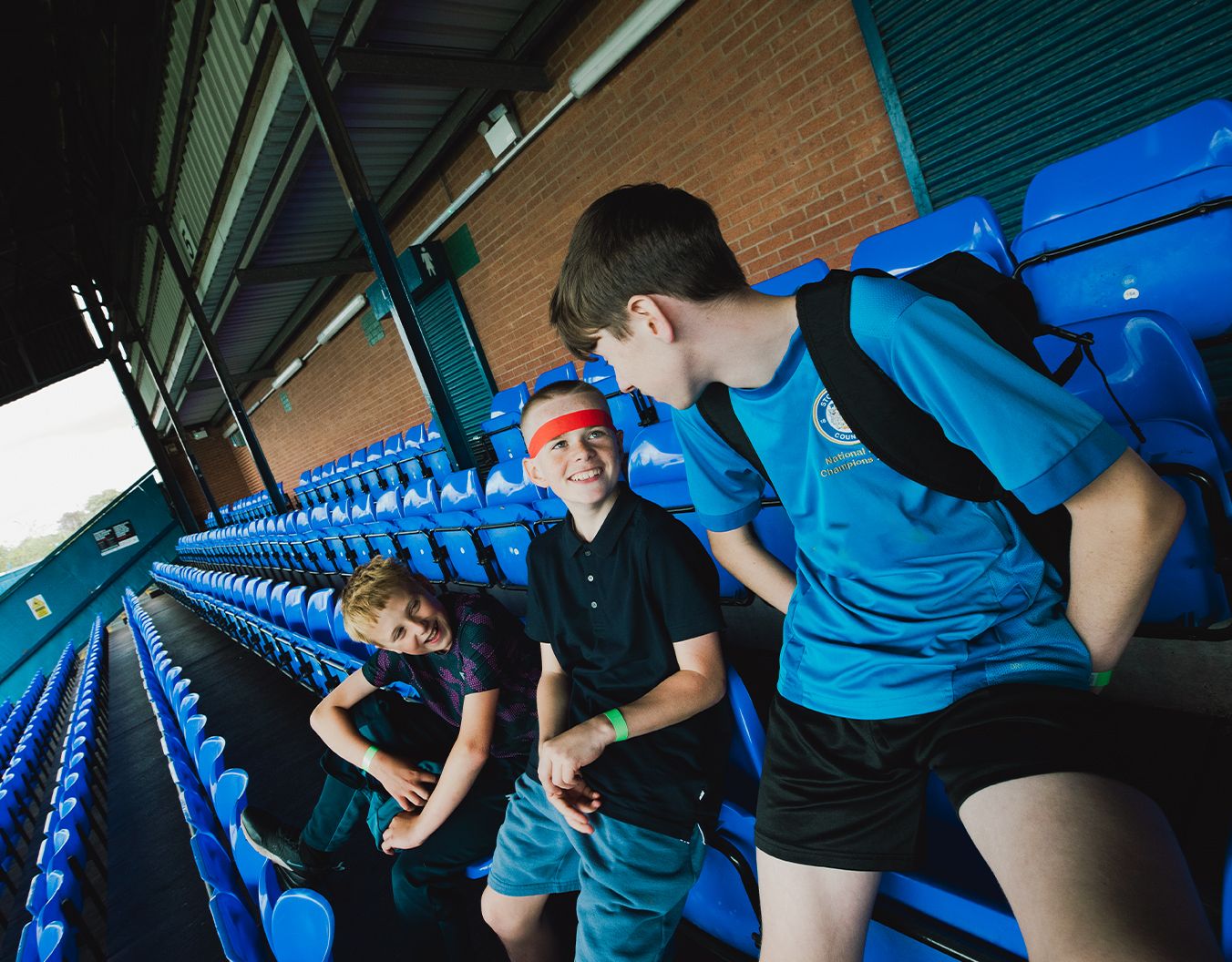 3 boys sat on seats in a stadium talking