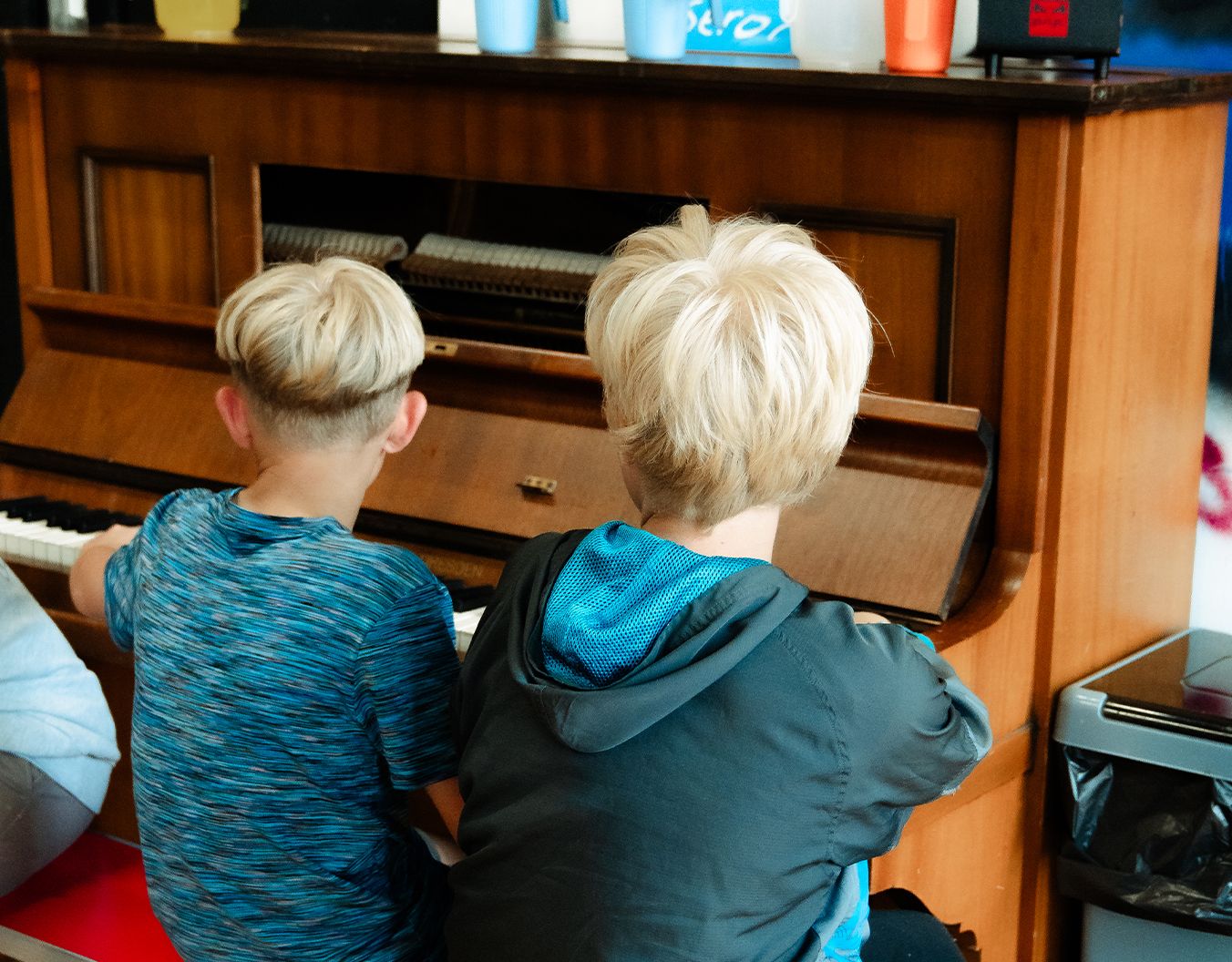A photo of the back of 2 blonde children's heads sat at a piano