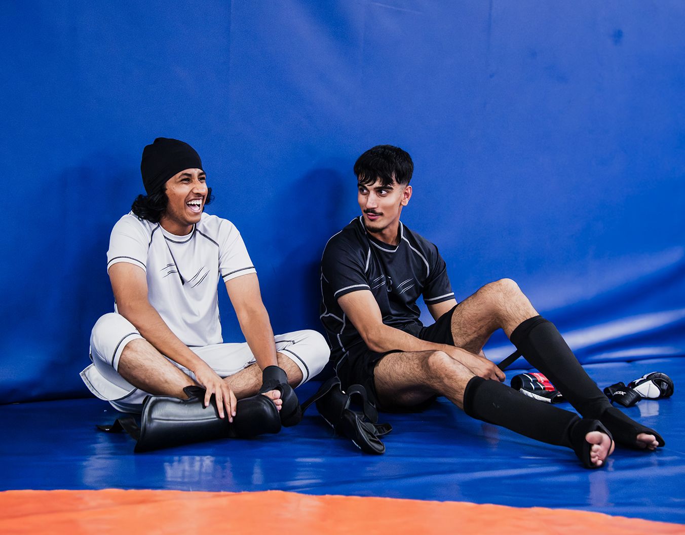 2 young adults sat on blue mats talking and laughing to eachother